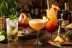 Vier rumcocktails op bar, waaronder mojito, pina colada-achtig en kleurrijke tequila sunrise-variant